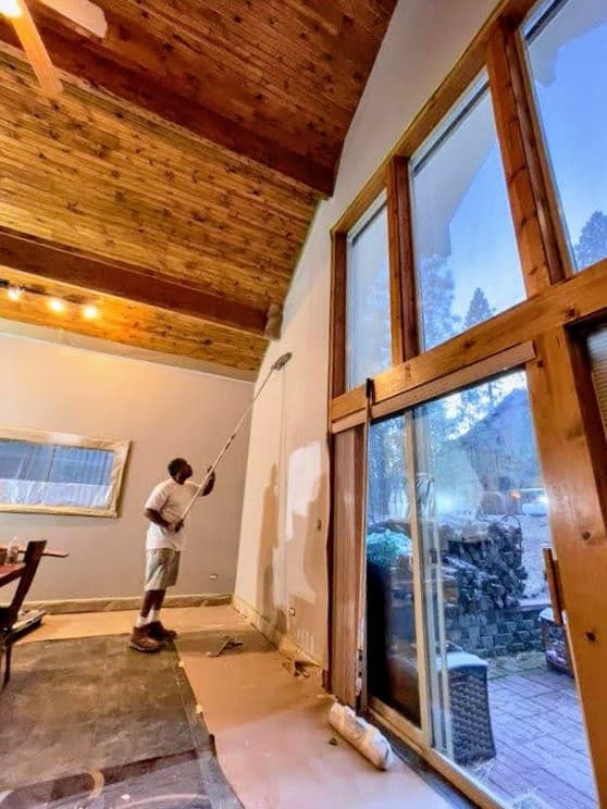 Painter rolling a vaulted interior wall beside wood windows